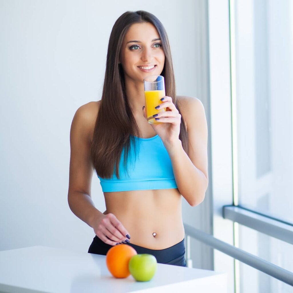 Toned and Fit looking woman in blue t shirt, drinking orange juice and eats apple boosting her metabolism.