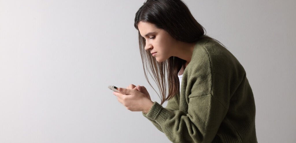 Side profile of a woman in a green sweater, intently focusing on her smartphone, holding a bad posture.