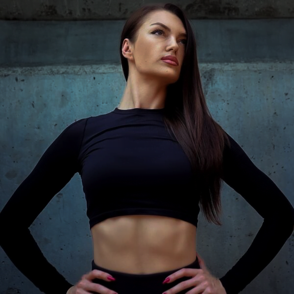 Elena: Fitness professional showcasing her physique against a concrete backdrop, highlighting advanced bodybuilding and personal training expertise.