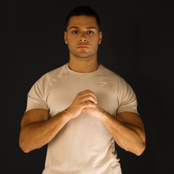 Meet Mena fitness, boxing & kickboxing certified coach. Standing in dark background with his hands crossed