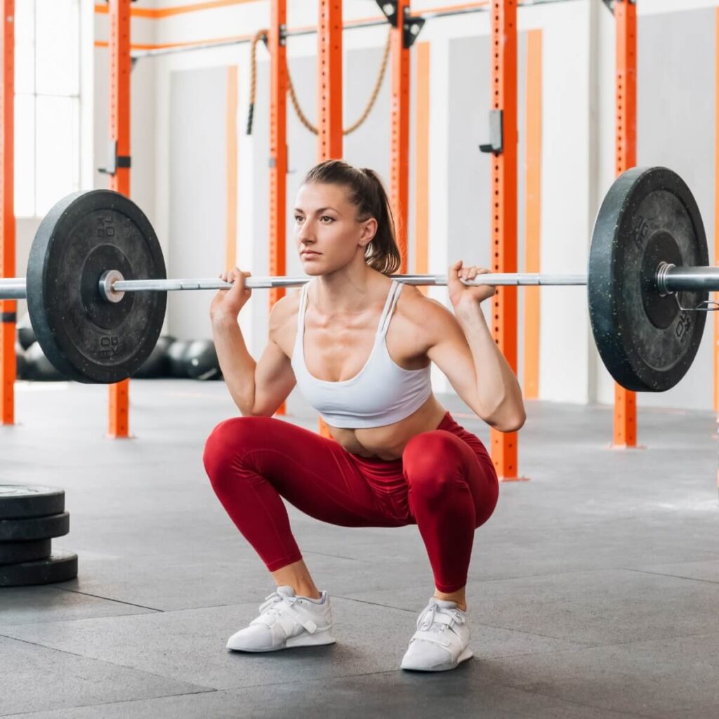 Woman in white t shirt and red leggings performing full squat, sticking to old school workout approach