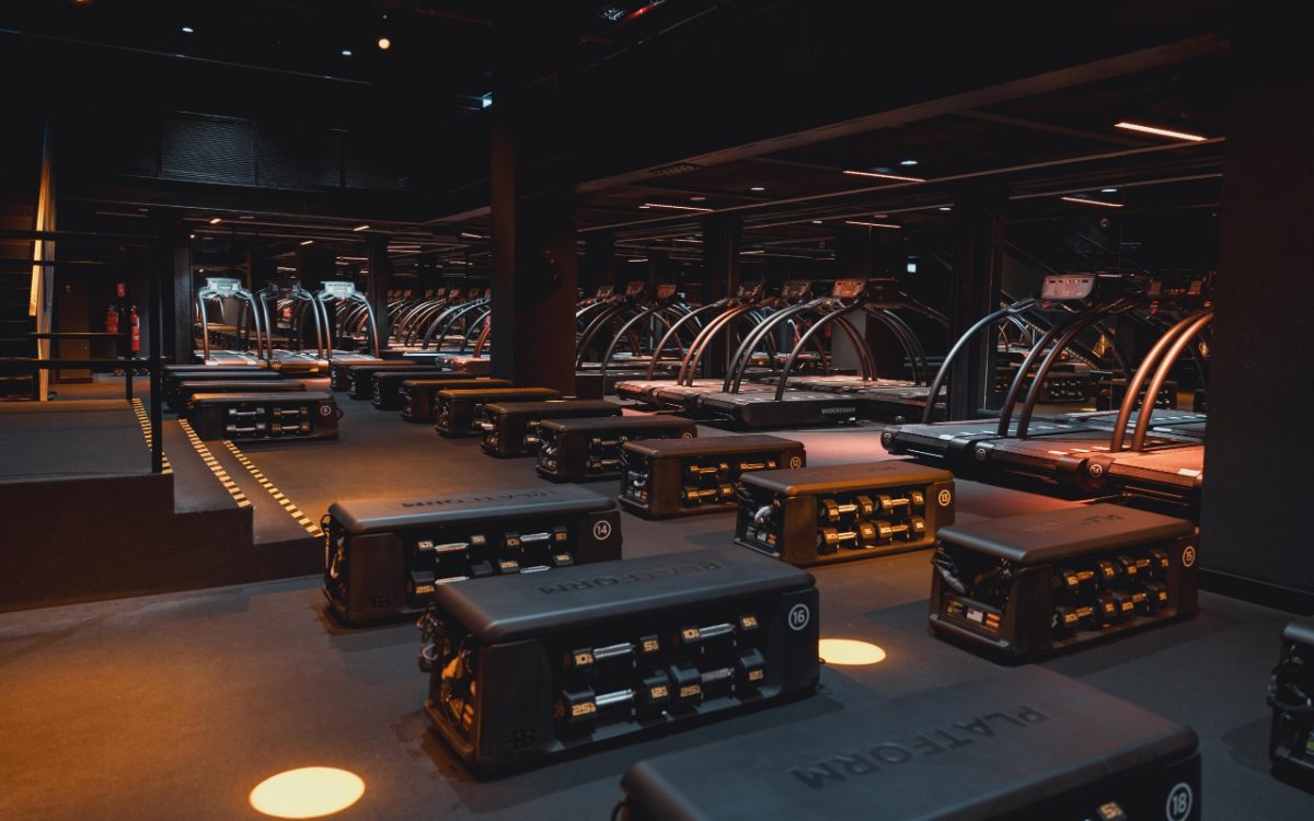 The gym floor at FitnGlam, with curved treadmills and workout benches with dumbbell racks