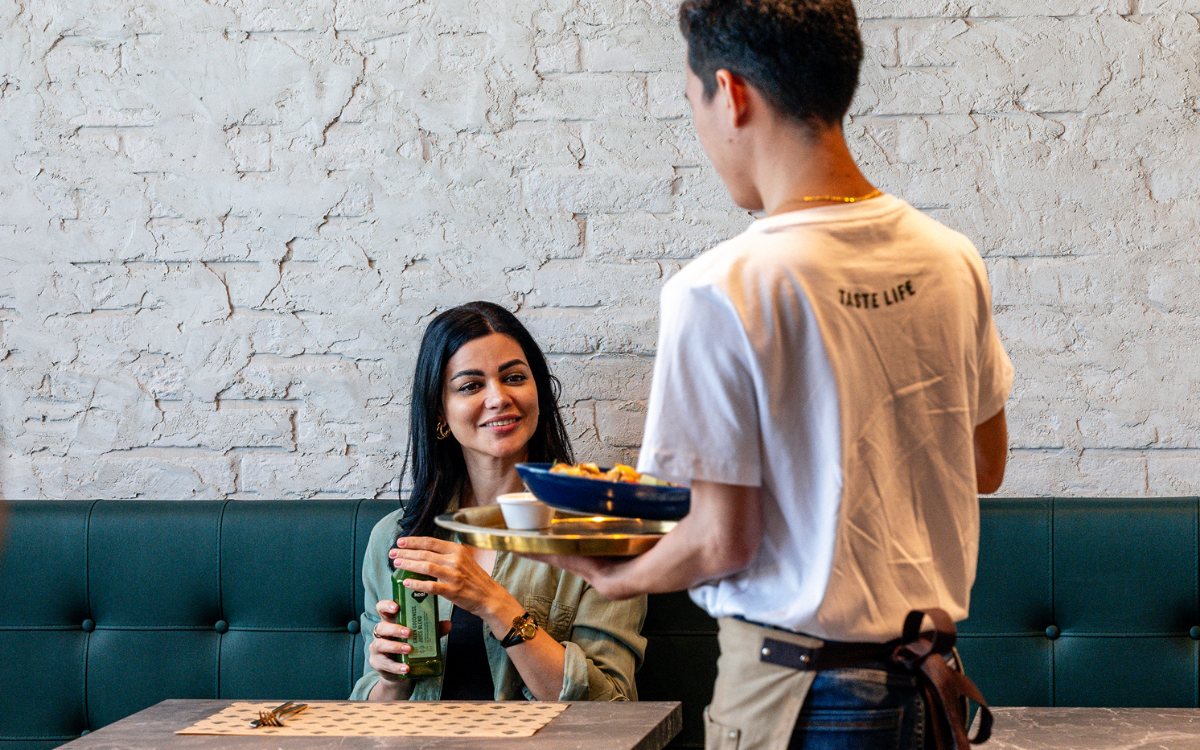 Inside a Kcal Life restaurant, a server bringing a bowl to a table